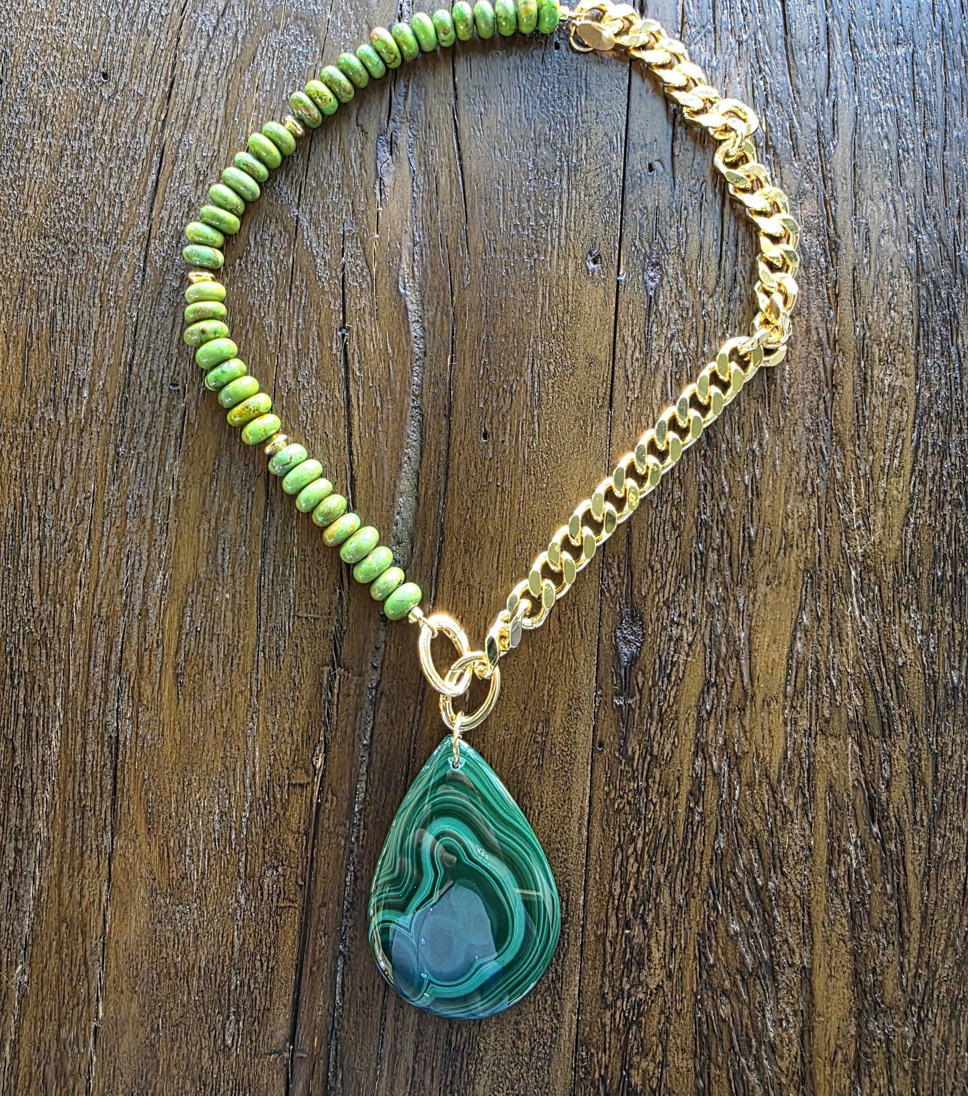 Necklace with green turquoise beaded chain and gold chain, featuring a green teardrop pendant on a wooden surface.